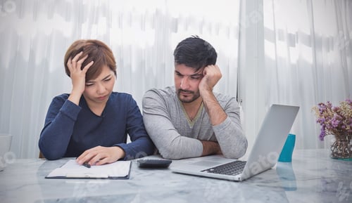 Preview: Portrait of worried couple paying bills online via laptop in living room at home