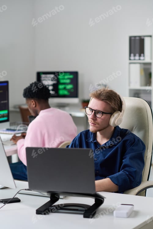 Preview: Young Man Wearing Headphones Working on Laptop in Office Setting