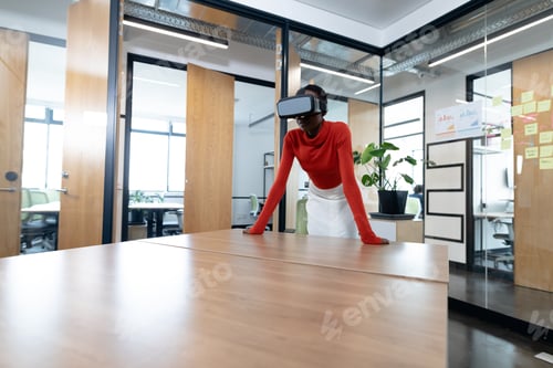Preview: African american businesswoman leaning on desk and using vr headset in meeting room