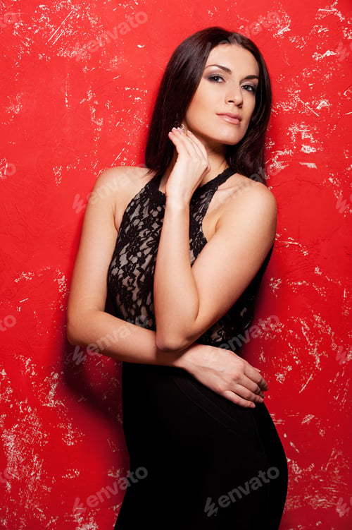 Preview: Beauty on red. Beautiful young woman in black dress posing against red background