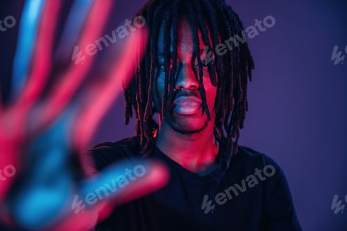 Preview: With hand in front of him, stop gesture. African American guy is studio with neon lighting