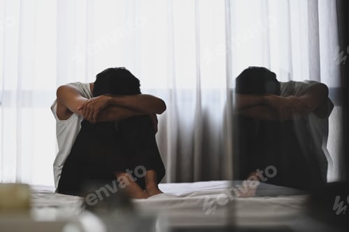 Preview: Depressed man sitting in the dark bedroom with low light environment.