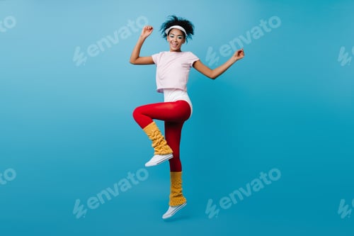 Preview: Graceful black girl doing aerobics. Gorgeous african woman jumping on blue background.