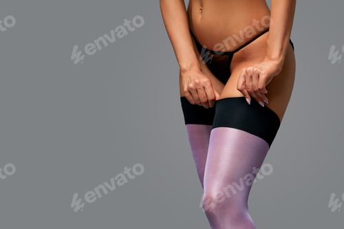 Preview: Girl puts stockings on legs on a gray background. The concept of women's underwear, seduction of men