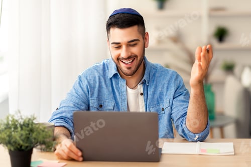 Preview: Smiling israeli man working on laptop computer at home