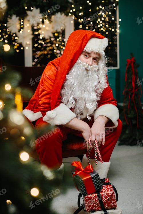 Preview: Santa claus holding candy canes and gifts posing next to christmas tree