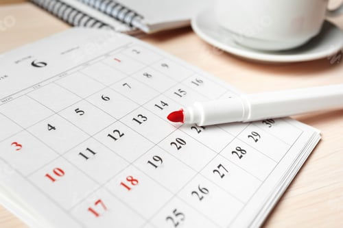 Preview: Red pen marking important dates on a calendar at a workspace with coffee