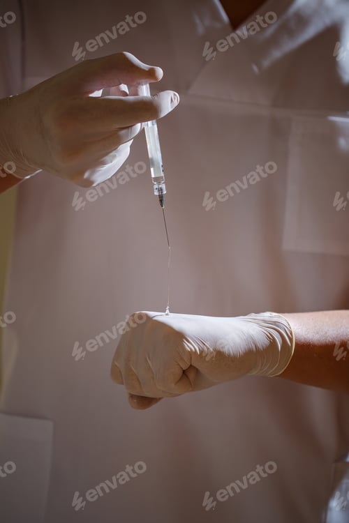Preview: Male doctor chief physician in a white surgical suit. Close-up portrait. Holds a syringe