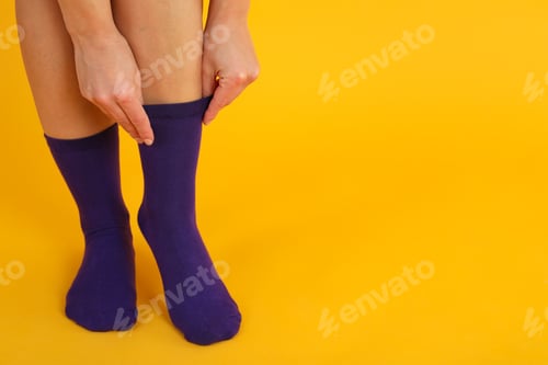 Preview: Woman pull up socks on yellow background