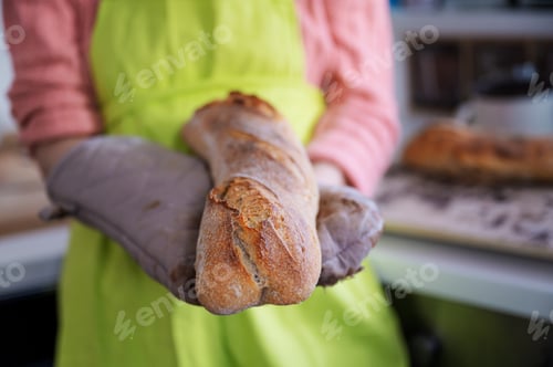 Preview: Woman in green apron holding her home made sourdough baguette