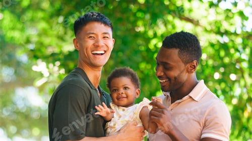 Preview: Joyful Family Moment With Two Fathers Holding Their Baby in a Park During Daytime