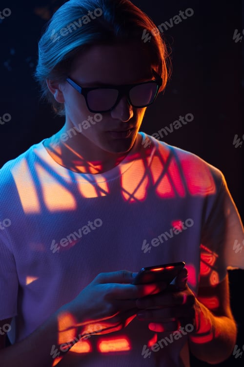 Preview: Stylish man using smartphone under red light