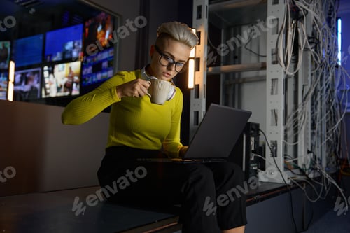 Preview: Young hipster woman working with laptop in server room