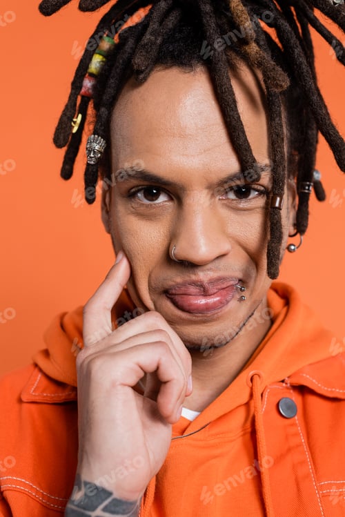 Preview: portrait of tattooed and multiracial man with dreadlocks smiling isolated on coral