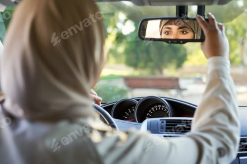Preview: Young Muslim woman adjusting rearview mirror in car