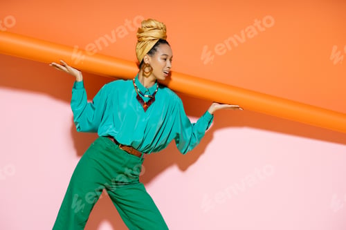 Preview: Smiling african american woman in trendy summer outfit posing on pink and orange background
