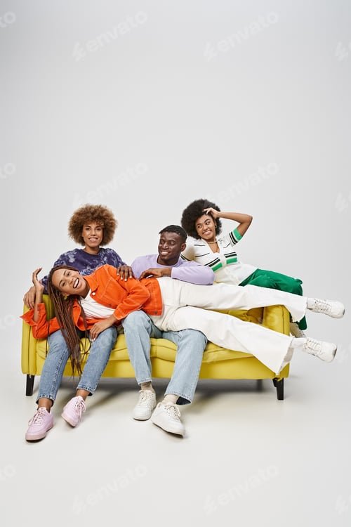 Preview: positive african american woman with dreadlocks lying on laps of friends sitting on yellow couch
