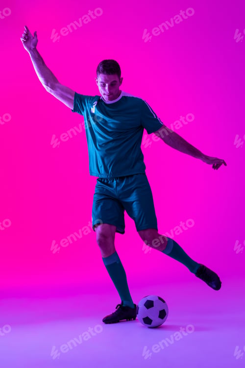 Preview: Caucasian male soccer player kicking football over neon pink lighting