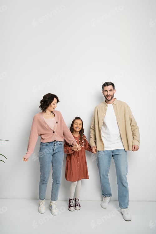 Preview: Smiling parents and kid holding hands on white background