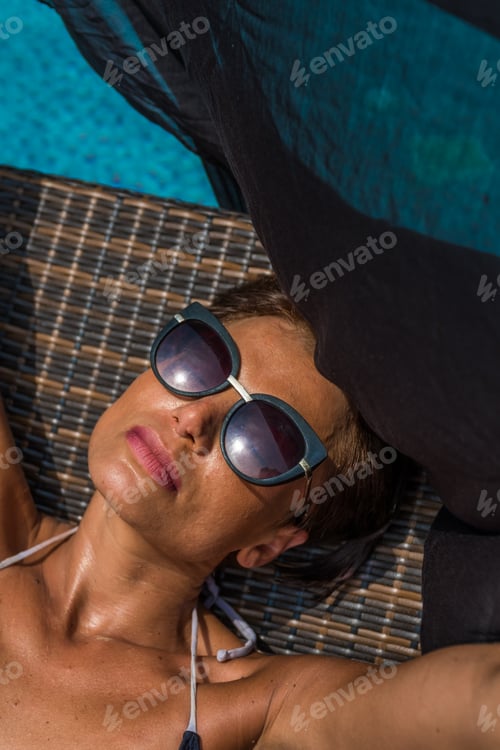 Preview: beautiful tanned young woman in bikini relaxing by the swimming pool.