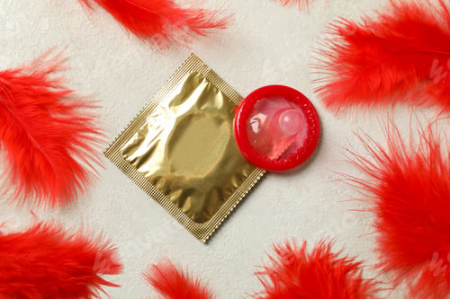 Preview: Condoms and red feathers on white textured background