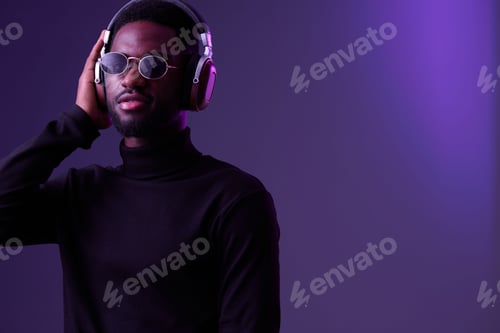 Preview: Stylish young man wearing sunglasses and headphones, enjoying music against a purple background