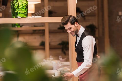 Preview: Handsome smiling waiter serving cup of coffee on a table