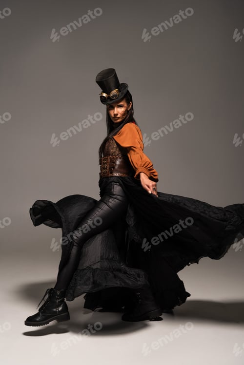 Preview: full length view of attractive steampunk woman in top hat with goggles on grey