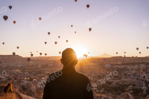Preview: Rear view of a male enjoying the sunrise and hot air balloons rising up in Cappadocia, Turkey