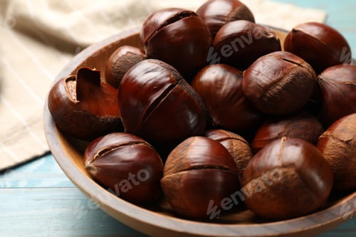 Preview: Fresh edible sweet chestnuts in bowl on light blue wooden table, closeup