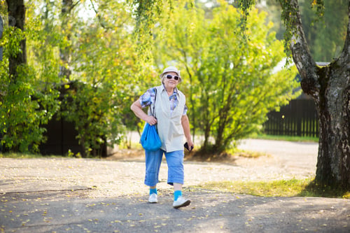 Preview: A smiling older woman with a shoulder bag and a camera goes on a hike