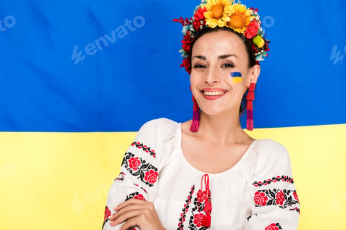 Preview: happy brunette young woman in national Ukrainian costume and floral wreath with flag of Ukraine on