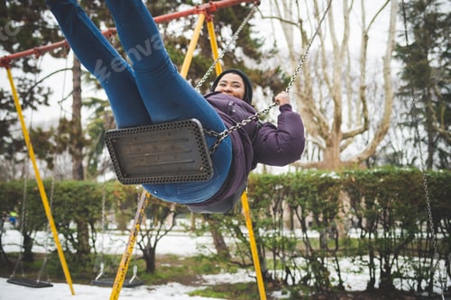 Preview: young african woman having fun on the swing outdoor in winter day