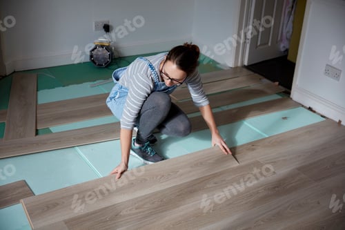 Preview: Woman laying new floorboards in the living room of a house under renovation.