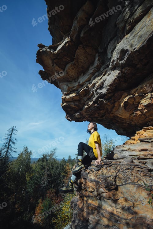 Preview: Climber sits on rock during bright day in forest area with clear sky