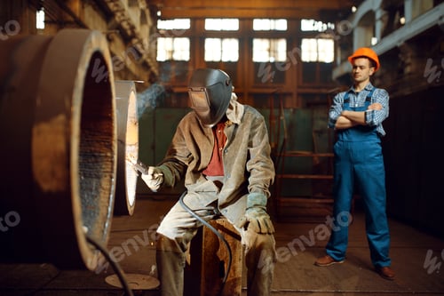 Preview: Welder works on factory, worker on background