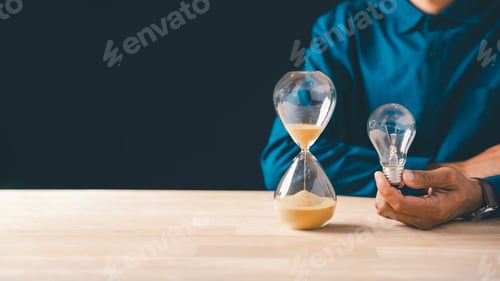 Preview: Hand holds clear lightbulb, sparking innovation idea for business growth, hourglass with flowing