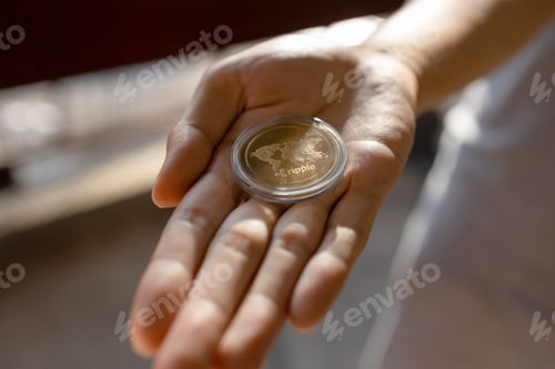Preview: Young man holding XRP Ripple coin on palm of hand