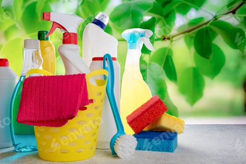 Preview: Basket with cleaning tools and products on blurry nature background. Spring cleaning