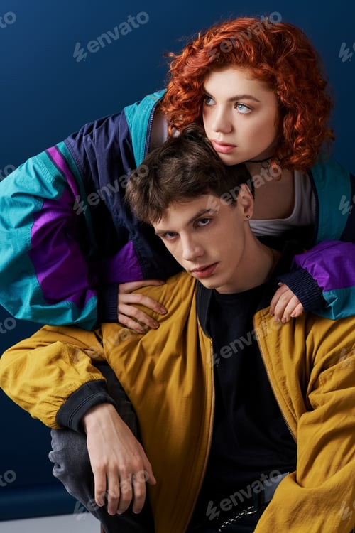 Preview: handsome boyfriend in colorful attire looking at camera next to his pretty red haired girlfriend