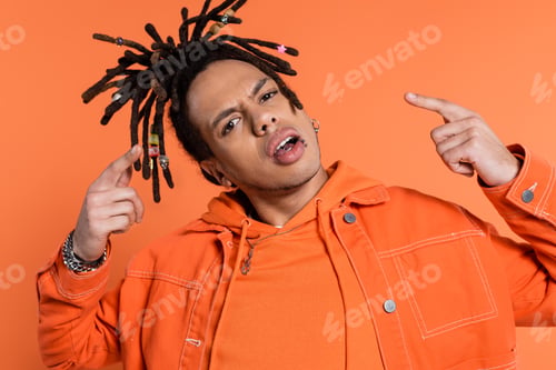 Preview: pierced and multiracial man with dreadlocks looking at camera while pointing with fingers isolated