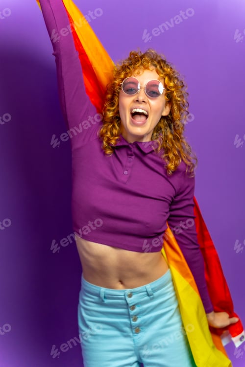 Preview: Cheerful young woman raising lgbt rainbow flag and smiling