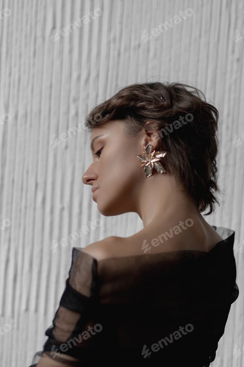 Preview: Model poses in a black outfit with bold earrings in a studio setting