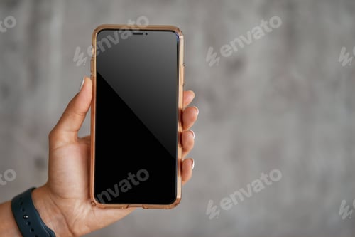 Preview: Female hand holding smartphone against grey wall, selective focus