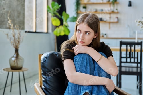 Preview: Sad unhappy thoughtful young woman sitting in armchair at home