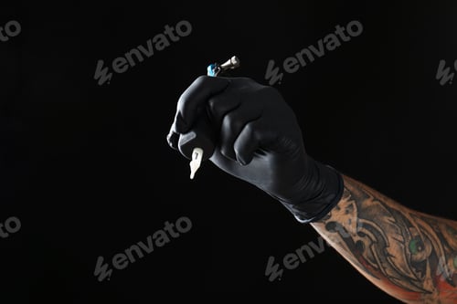 Preview: Professional tattoo artist with machine on black background, closeup. Space for text