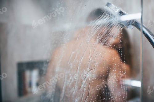 Visualização: Vista através do vidro de um jovem casal que se abraça e se beija no banheiro