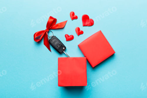 Preview: Black car key in a present box with a ribbon and red heart on colored background.