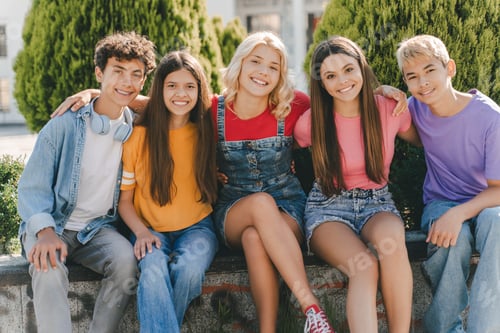Preview: Group of smiling friends, multiracial teenagers hugging, sitting outdoors. Friendship