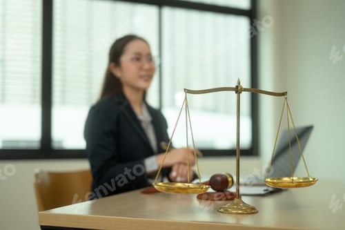 Preview: Golden balance scales on wooden table against professional lawyer in background.